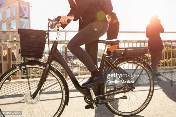 low section of mature woman riding electric bicycle by commuters on bridge in city against sky - electric bike stockfoto's en -beelden