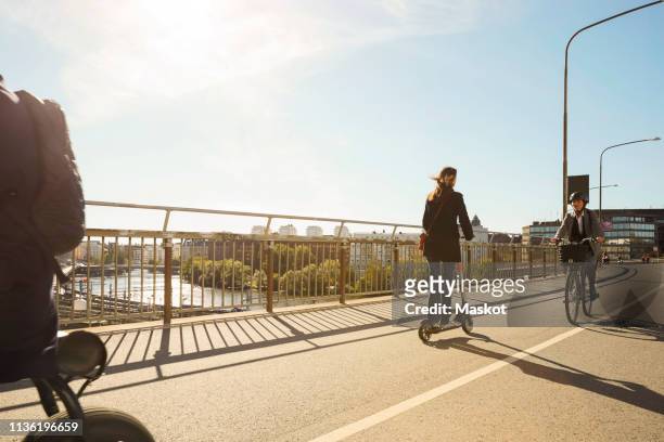 Commuters riding electric vehicles on bridge against blue sky