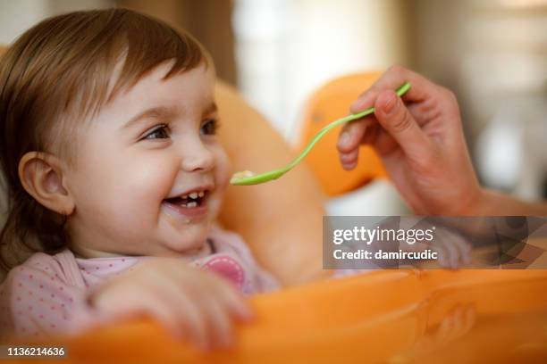 mutter fütterung glückliches kleinkind mädchen mit einem löffel - baby eating stock-fotos und bilder