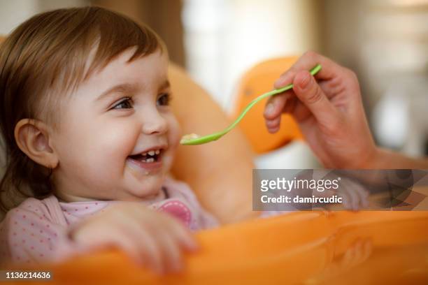 madre alimentando niña feliz niño con una cuchara - bebe 1 a 2 años fotografías e imágenes de stock