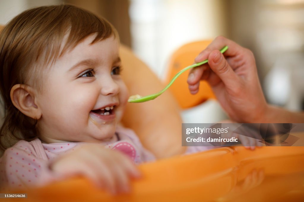 Mother feeding happy toddler girl with a spoon