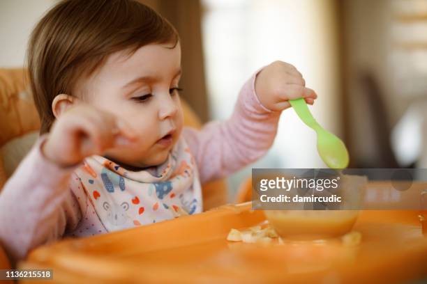 little baby girl eating food on high chair - spoon in hand stock pictures, royalty-free photos & images