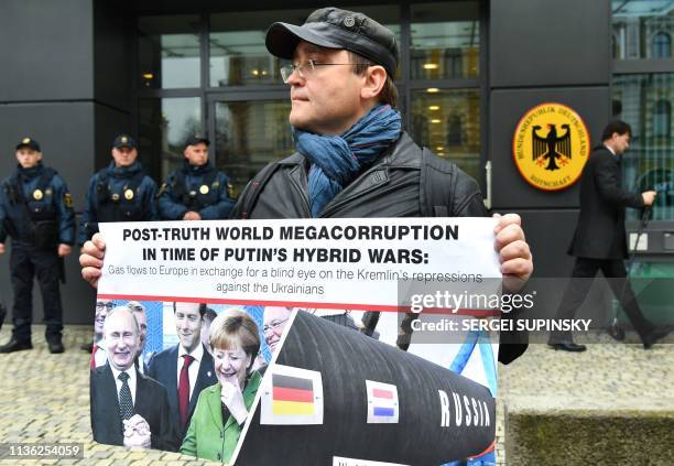 Man holds a placard depicting Russian President Vladimir Putin and German Chancellor Angela Merkel smiling, and the Nord Stream 2 gas pipe-line,...