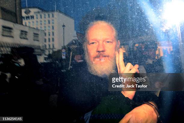 Julian Assange gestures to the media from a police vehicle on his arrival at Westminster Magistrates court on April 11, 2019 in London, England....