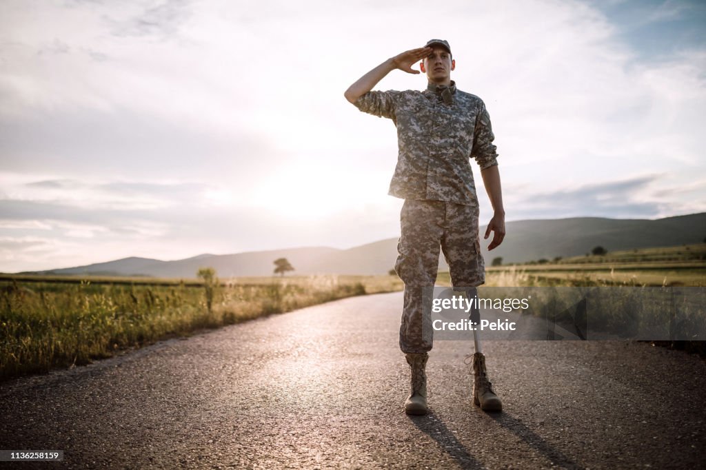 Brave soldier with prosthetic leg saluting on road