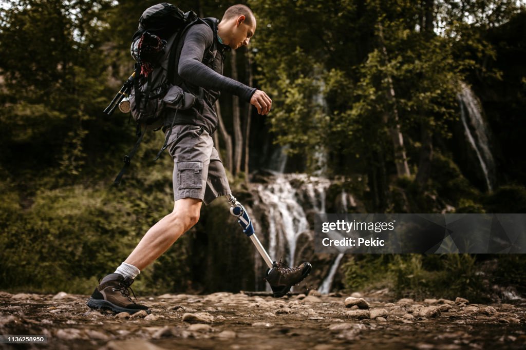 Man with disability crossing stream in forest