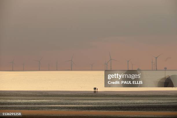 People walk on the beach at New Brighton, north west England at sunset on April 11 with the Burbo Bank wind farm on the Irish Sea in the background.