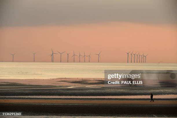 People walk on the beach at New Brighton, north west England at sunset on April 11 with the Burbo Bank wind farm on the Irish Sea in the background.