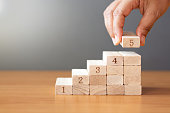 Women hand putting a wooden block on top and arranging wooden blocks stacking on wooden table.