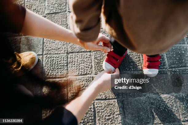 mother helping her daughter to put on her shoes in the park - boy tying shoes stock-fotos und bilder