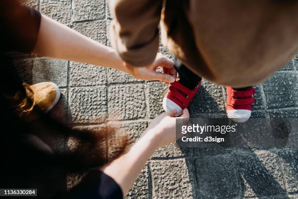 mother helping her daughter to put on her shoes in the park - ties stock pictures, royalty-free photos & images