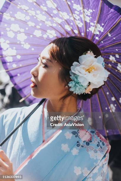 beautiful woman in traditional kimono holding umbrella looking towards sky under the warmth of sunlight - holding umbrella stock pictures, royalty-free photos & images