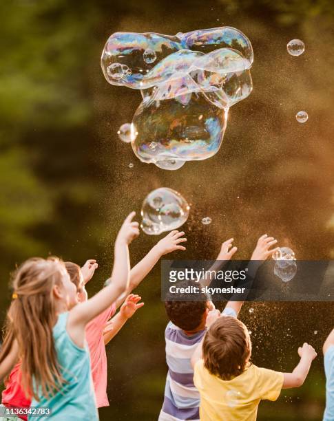 group of kids having fun while playing with rainbow bubbles in the park. - catching bubbles stock pictures, royalty-free photos & images
