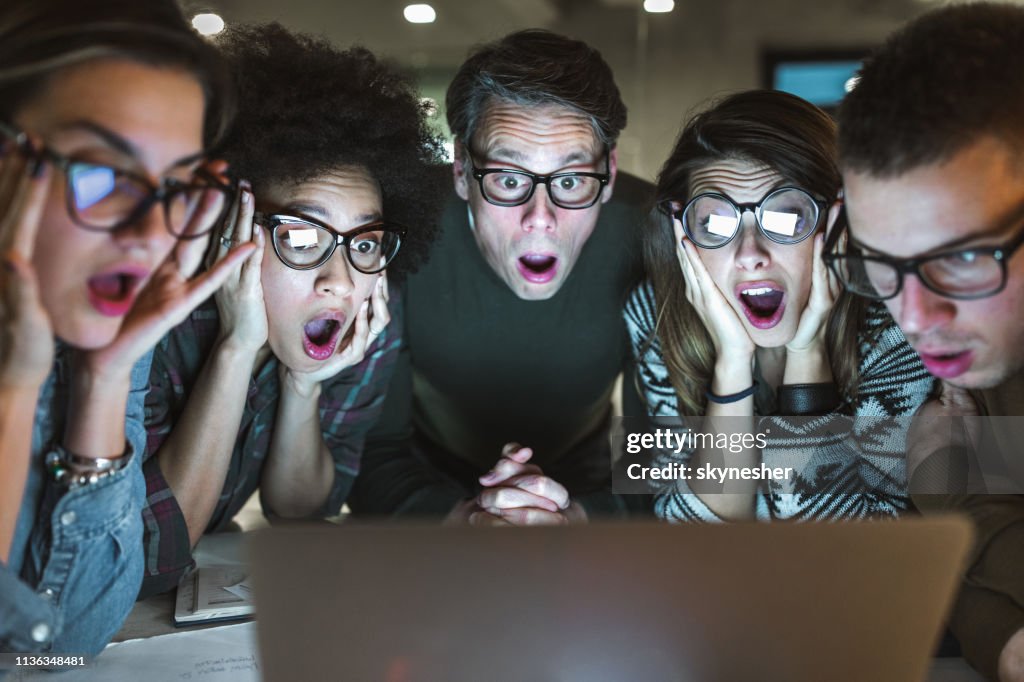 Schockiertes Team von Unternehmern, die eine E-Mail auf Laptop im Büro lesen.