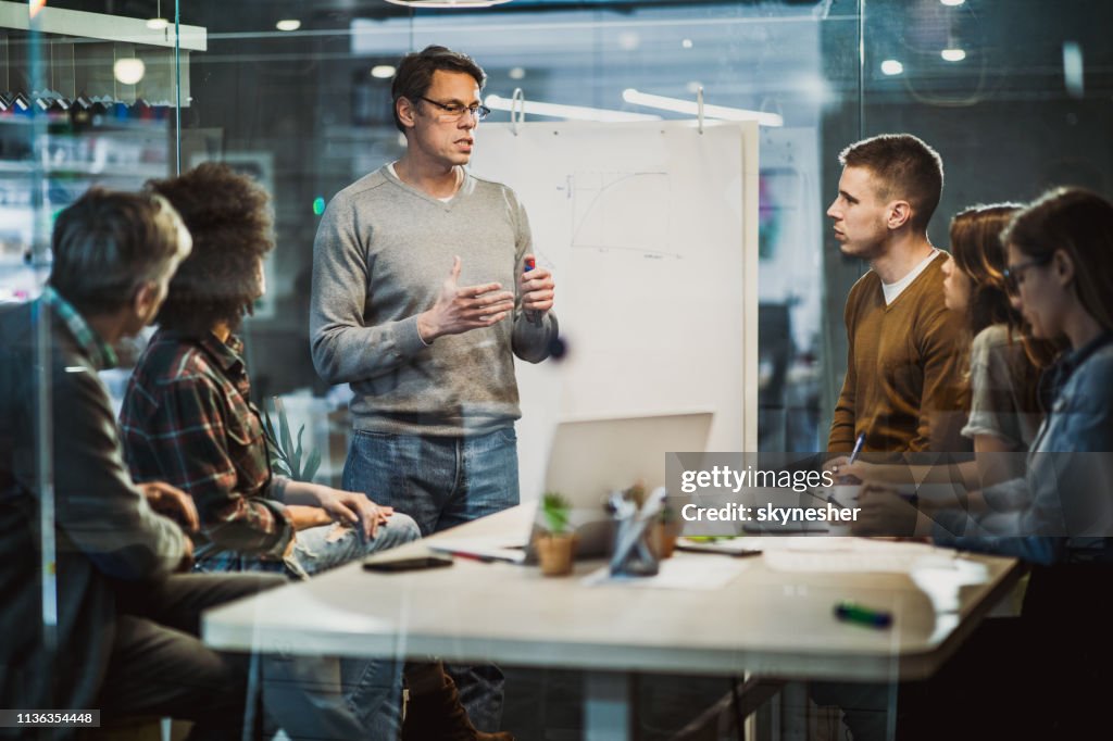 Mid adult businessman talking to his colleagues on presentation in the office.