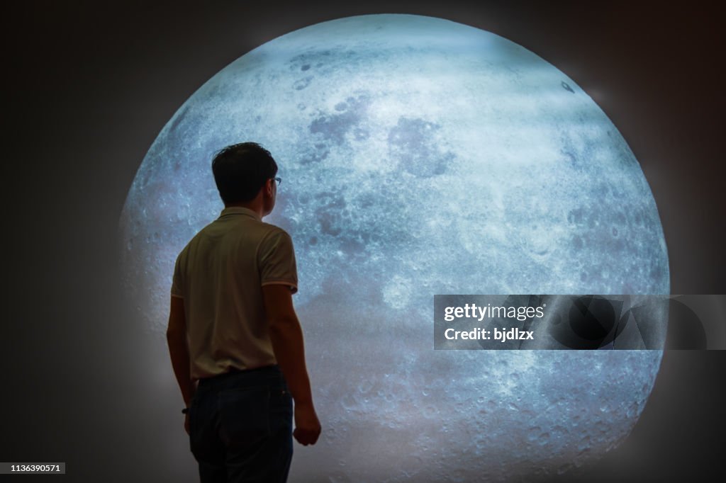 Asian Man Looking At Full Moon In Sky At Night