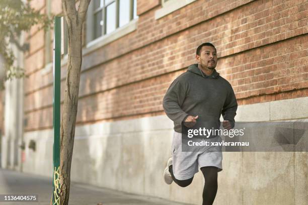 atleta masculino confiado corriendo en la acera en la ciudad - hombre gordo fotografías e imágenes de stock