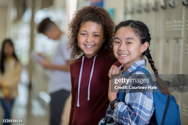 diverse ragazze delle scuole medie che sorridono alla telecamera nel corridoio vicino agli armadietti prima della lezione - educazione secondaria di scuola media foto e immagini stock