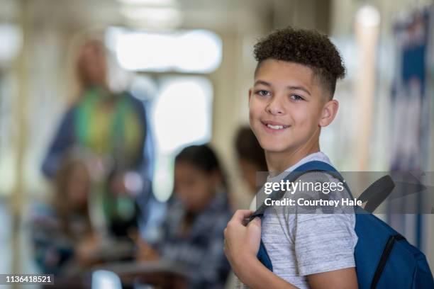 中学校の少年は廊下でクラスに歩いている間、カメラで笑顔 - 中学校 ストックフォトと画像