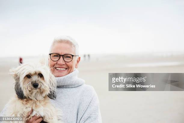 portrait of a content and happy senior woman at the beach with her dog - happy lady walking dog stockfoto's en -beelden