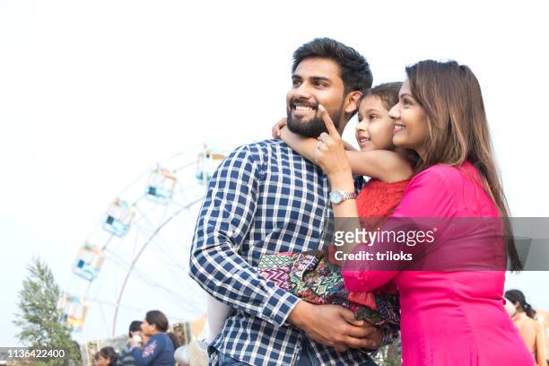 happy family standing in front of ferris wheel - indian ethnicity family stock pictures, royalty-free photos & images