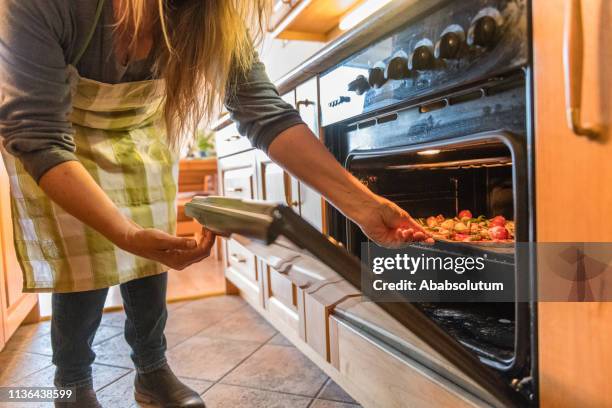 senior woman putting vegetarian pizza into the oven - vegetarian pizza stock pictures, royalty-free photos & images