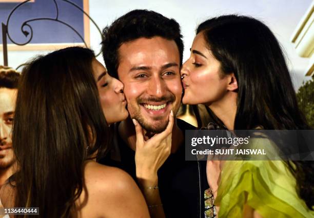 Indian Bollywood actresses Tara Sutaria and Ananya Pandey kiss on the cheeks of actor Tiger Shroff as they pose for photographs during the trailer...
