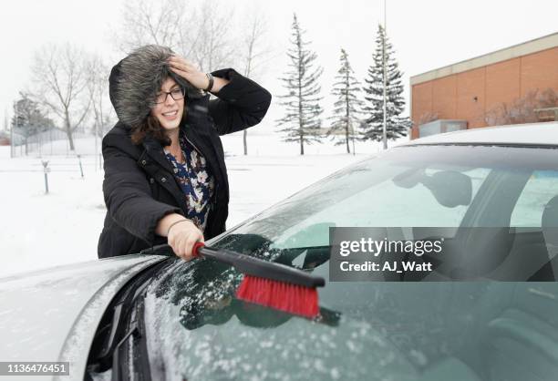 sweeping snow off her car window - winter car window stock-fotos und bilder