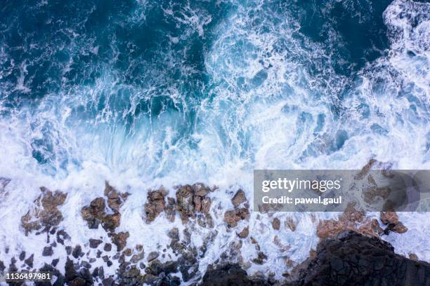 aerial view of ocean waves breaking on rocky beach - shallow stock pictures, royalty-free photos & images