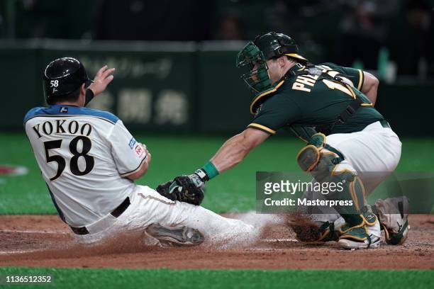 Toshitake Yokoo of the Hokkaido Nippon-Ham Fighters is tagged out by Catcher Josh Phegley of the Oakland Athletics in the bottom of 7th inning during...