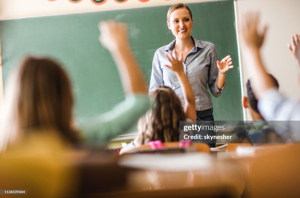 Glückliche Grundschullehrerin stellte eine Frage zu einer Klasse in der Schule.