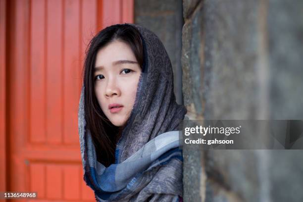 ritratto ravvicinato di una giovane donna dell'asia orientale con velo, in piedi accanto a una struttura di costruzione con porta arancione come sfondo - cultura dellasia orientale foto e immagini stock