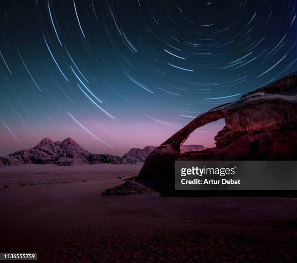 long exposure of the stars in the wadi rum desert of jordan with natural arch. - pose longue photos et images de collection