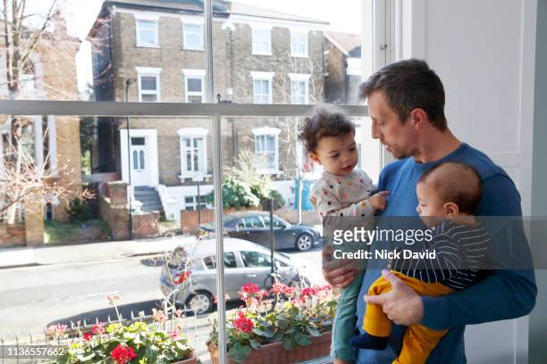 Single father holding baby son and daughter by window