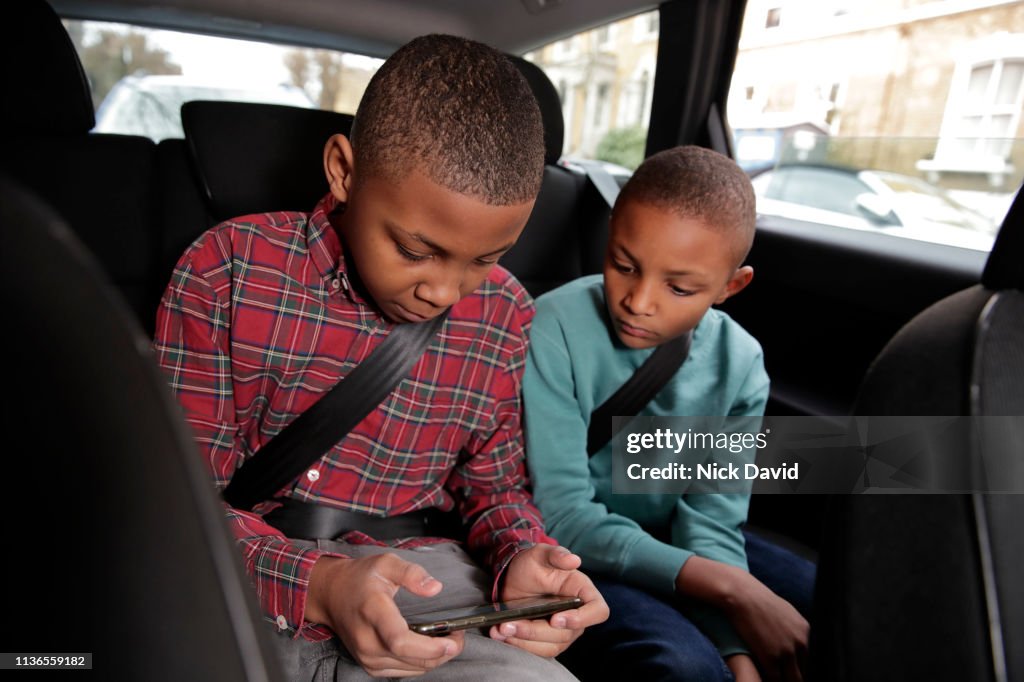 Brothers in back seat of car looking down at digital device