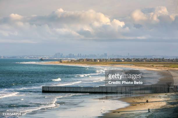 the us-mexico border wall along the pacific coast of tijuana with the san diego skyline on the horizon - mexico skyline stock pictures, royalty-free photos & images