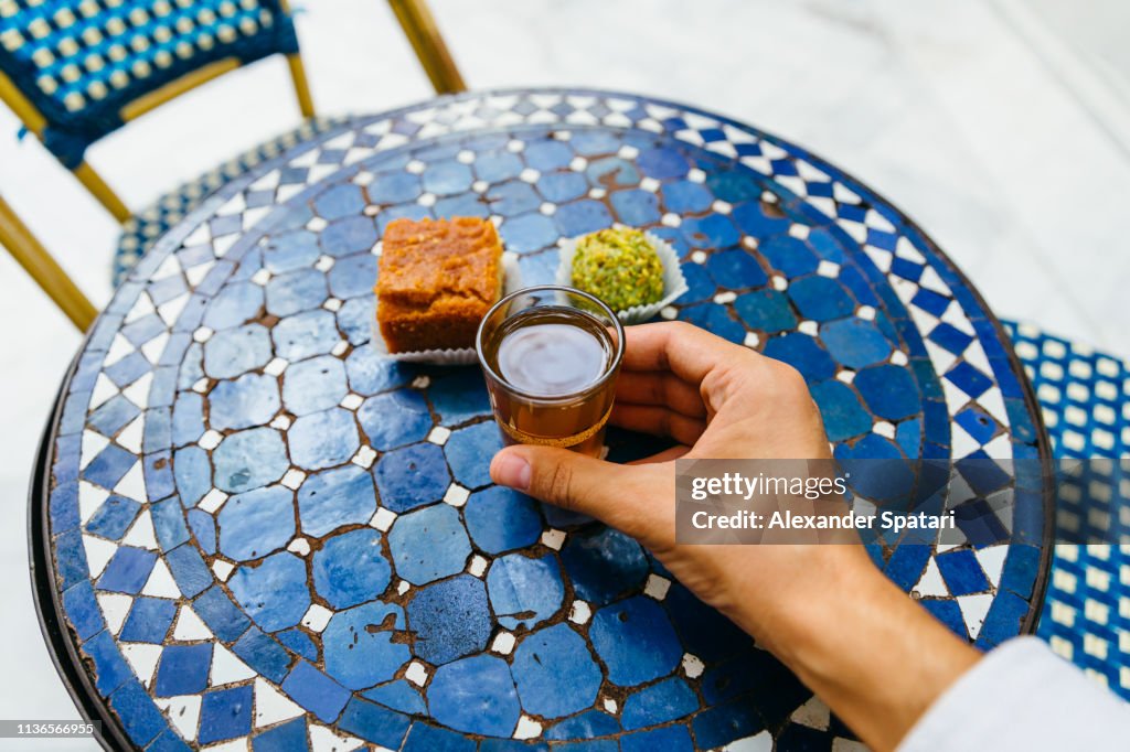 Personal perspective of man drinking sweet tea with Morrocan pastries at cafe