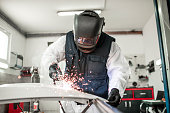 Body repair technician using a MIG welder to repair a damaged car part in a body shop