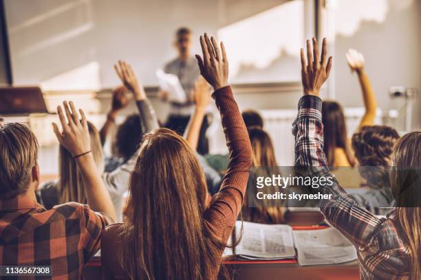 back view van de studenten het verhogen van de handen op een klas in collegezaal. - armen omhoog stockfoto's en -beelden