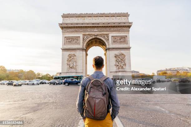tourist with backpack walking towards arc de triomphe in paris, france - paris france stock-fotos und bilder