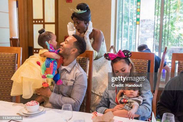 In this handout image, John Legend, Chrissy Teigen, their daughter Luna and son Miles share a moment with Princess Tiana during the Disney Princess...