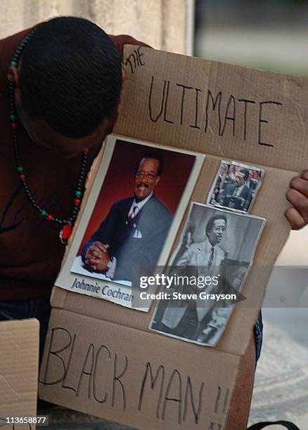 Participant in the candlelight vigil for bows his head as he holds a cardboard with images of the late attorney Johnnie L. Cochran at a candlelight...