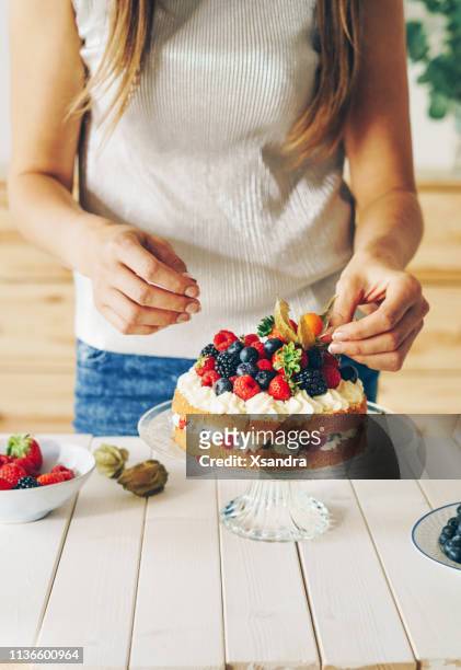 woman decorating a cake with fresh berries and physalis - layer cake stock pictures, royalty-free photos & images