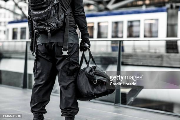 dark hooded terrorist figure at public transport hub - terrorism stock pictures, royalty-free photos & images