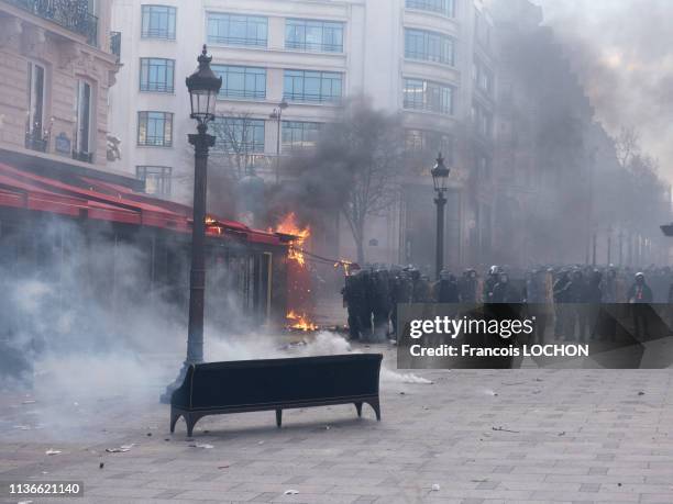 Force de l'ordre devant la vitrine brisée du restaurant le Fouquet's en flamme lors de la manifestation de l'acte 18 des "Gilets Jaunes" le 16 mars...