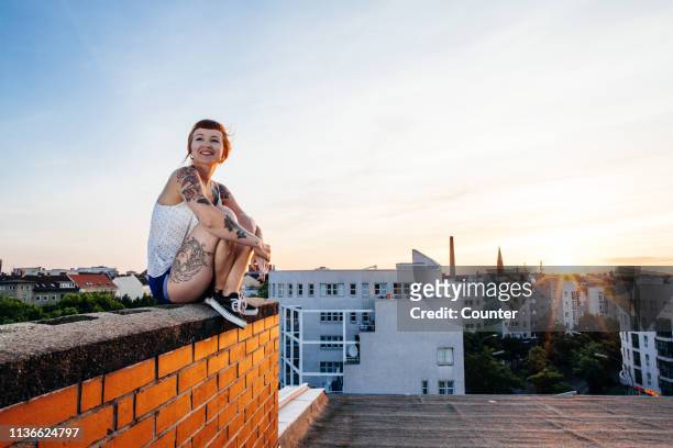 woman sitting on roof top - leben in der stadt stock-fotos und bilder