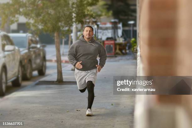 entschlossener männlicher sportler joggen auf bürgersteig in stadt - kräftig gebaut stock-fotos und bilder