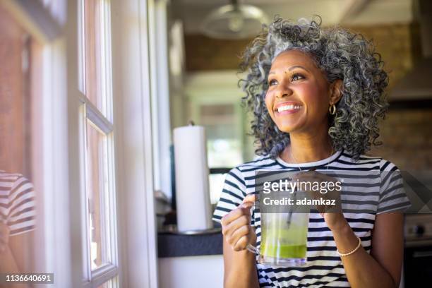 donna nera matura che beve un frullato verde - donne mature foto e immagini stock