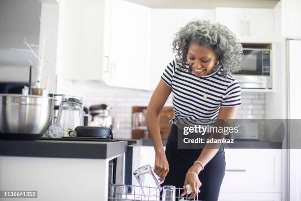 mature black woman loading dishwasher - loading dishwasher stock pictures, royalty-free photos & images