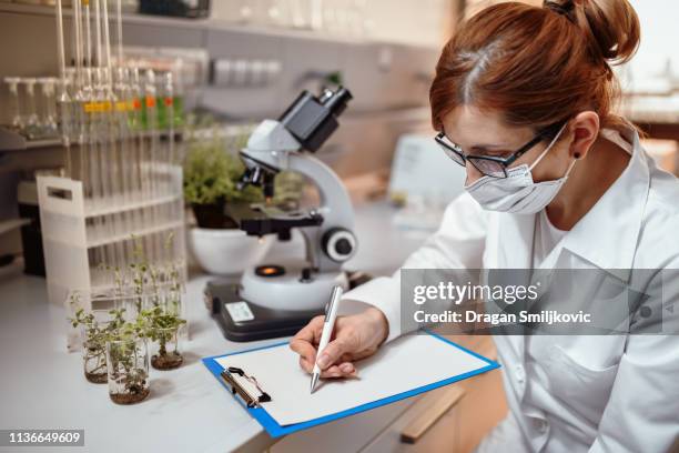 vrouwelijke wetenschapper maakt aantekeningen over het onderzoek - biochemie stockfoto's en -beelden